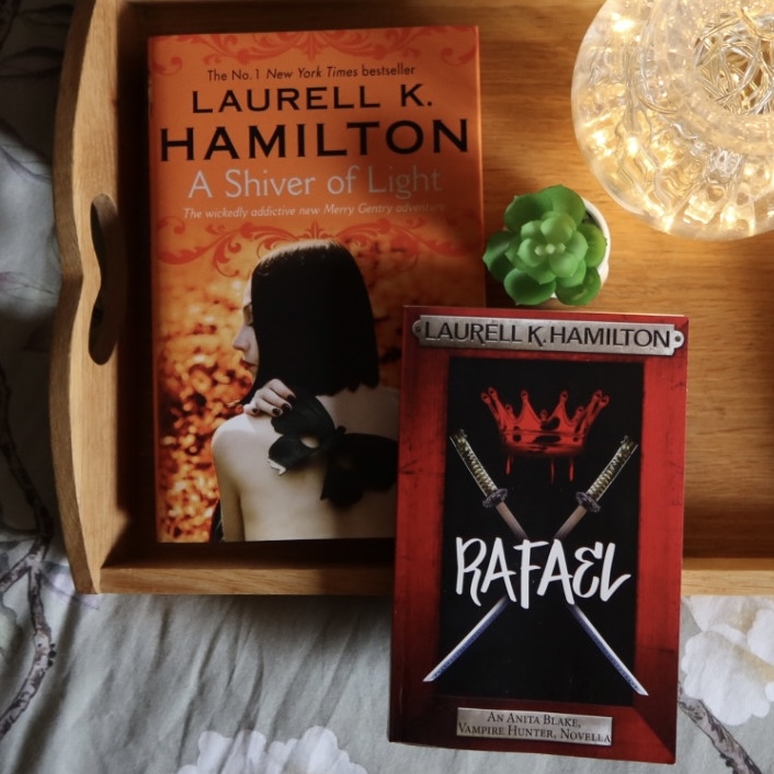 A photo of A Shiver of Light and Rafael both by Laurell K. Hamilton on a tray with a plant and a vase of lights